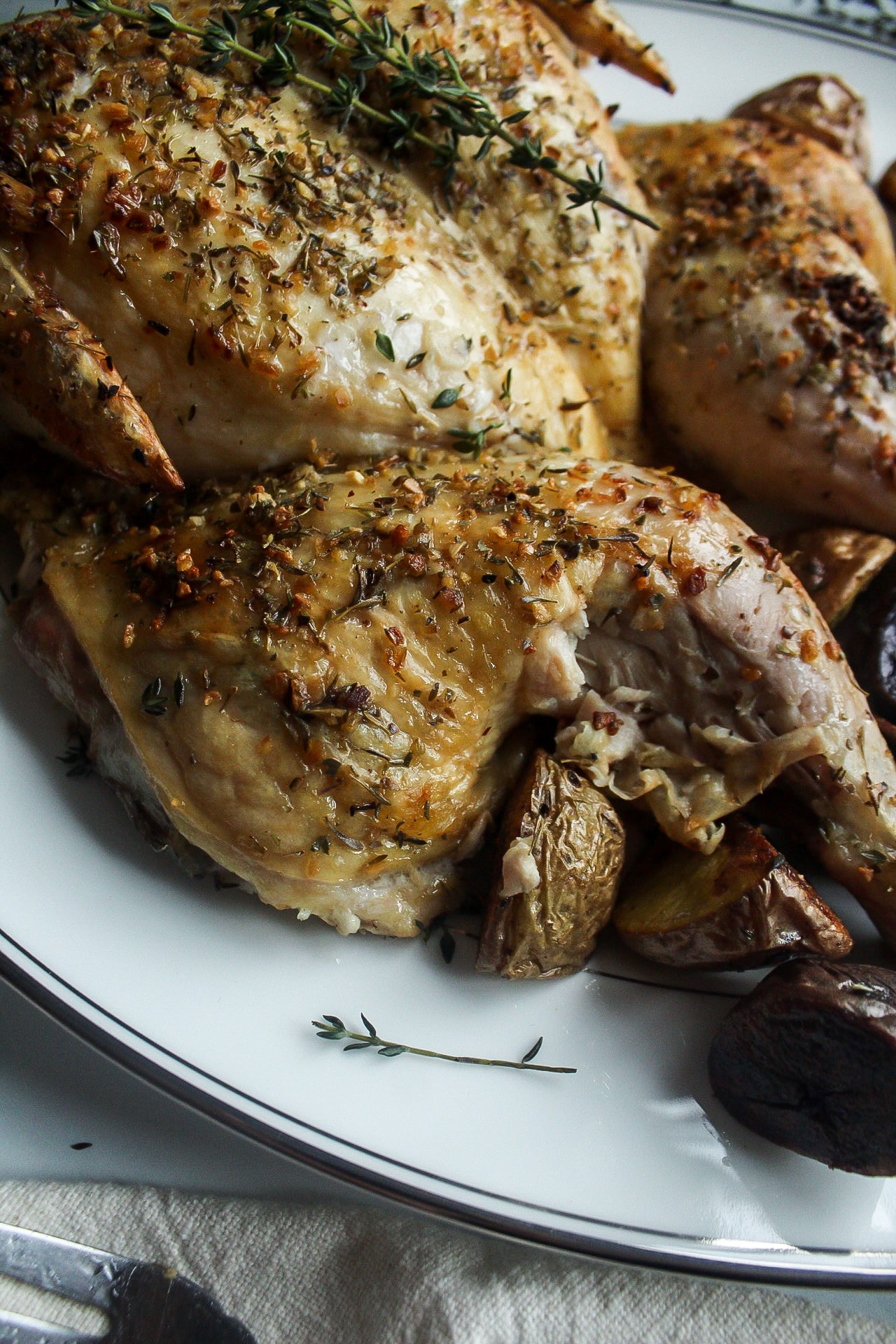 roasted leg of a whole roasted chicken on a patter with potatoes and herbs