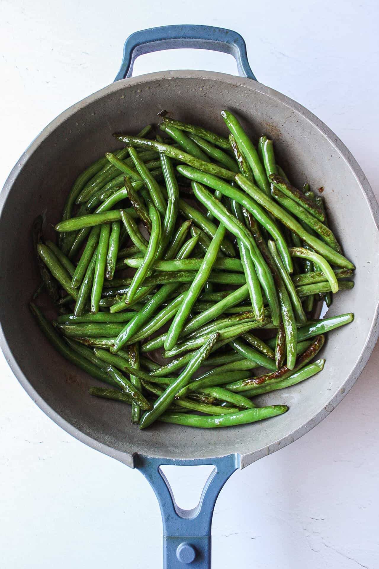 charred green beans in a skillet with olive oil