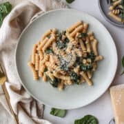 A plate of pasta with creamy spinach topped with Parmesan cheese