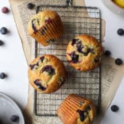four bakery style lemon blueberry muffins on a cooling rack.