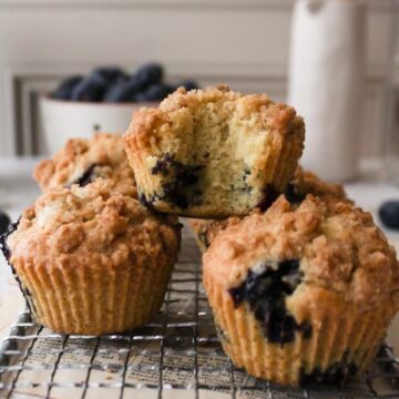 a stack of three muffins with one of them with a bite and blueberries int he background