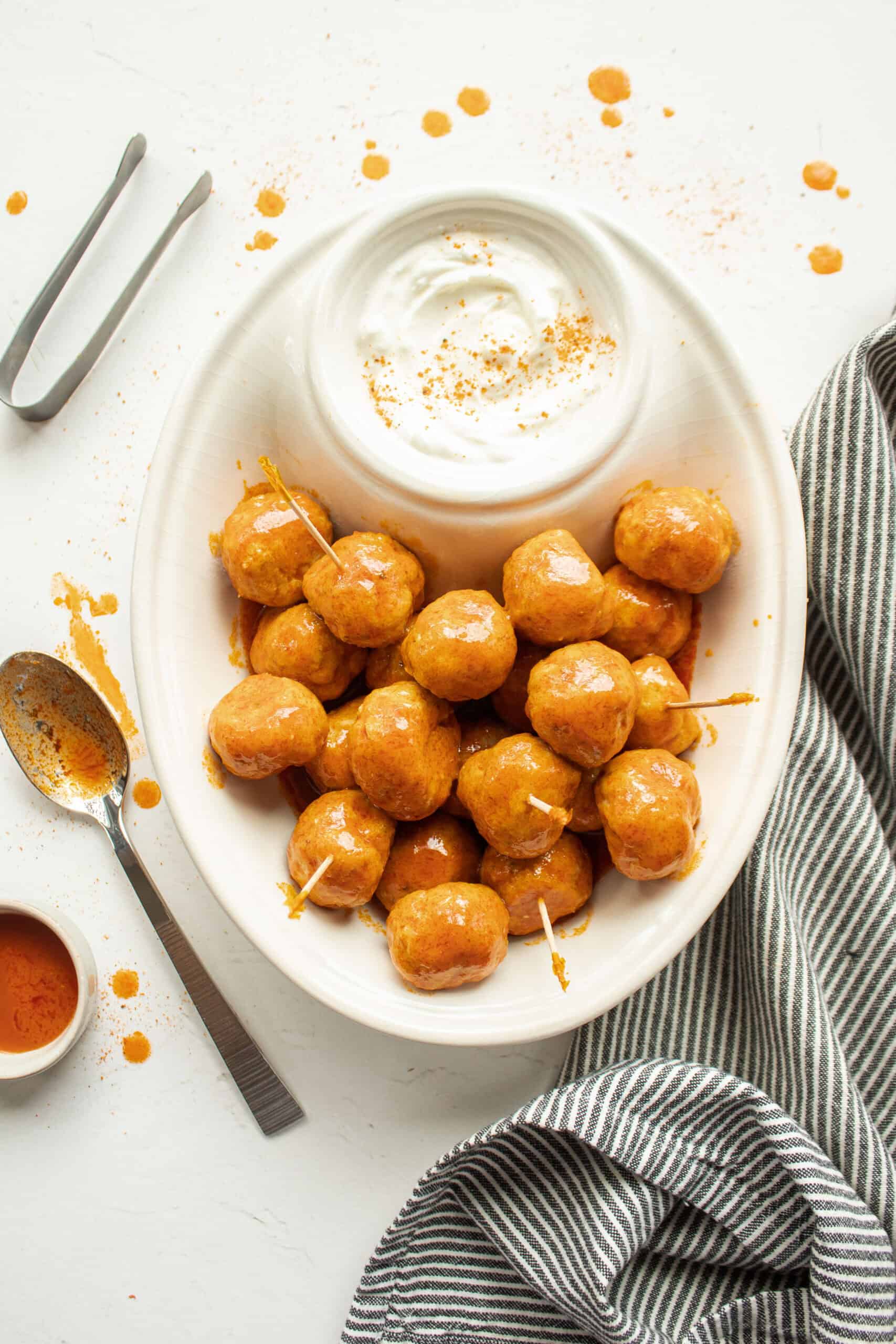 Buffalo chicken meatballs tossed in hot sauce in a platter with dipping sauce.