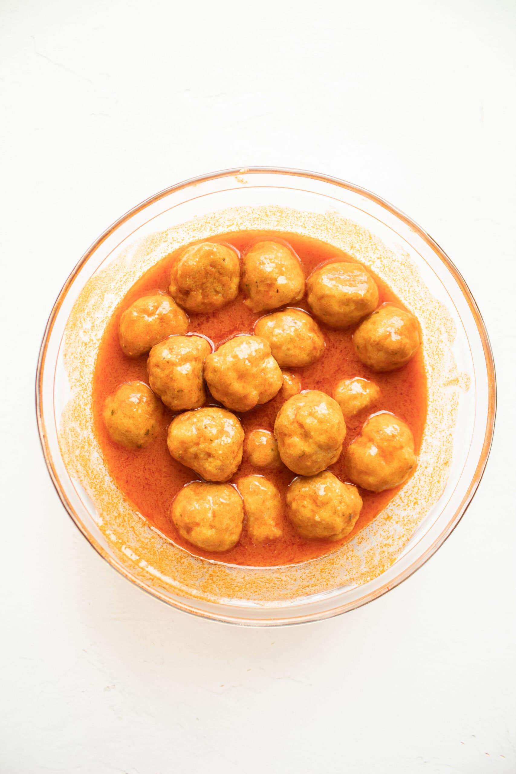 Mini buffalo chicken meatballs tossed in hot sauce in a mixing bowl.