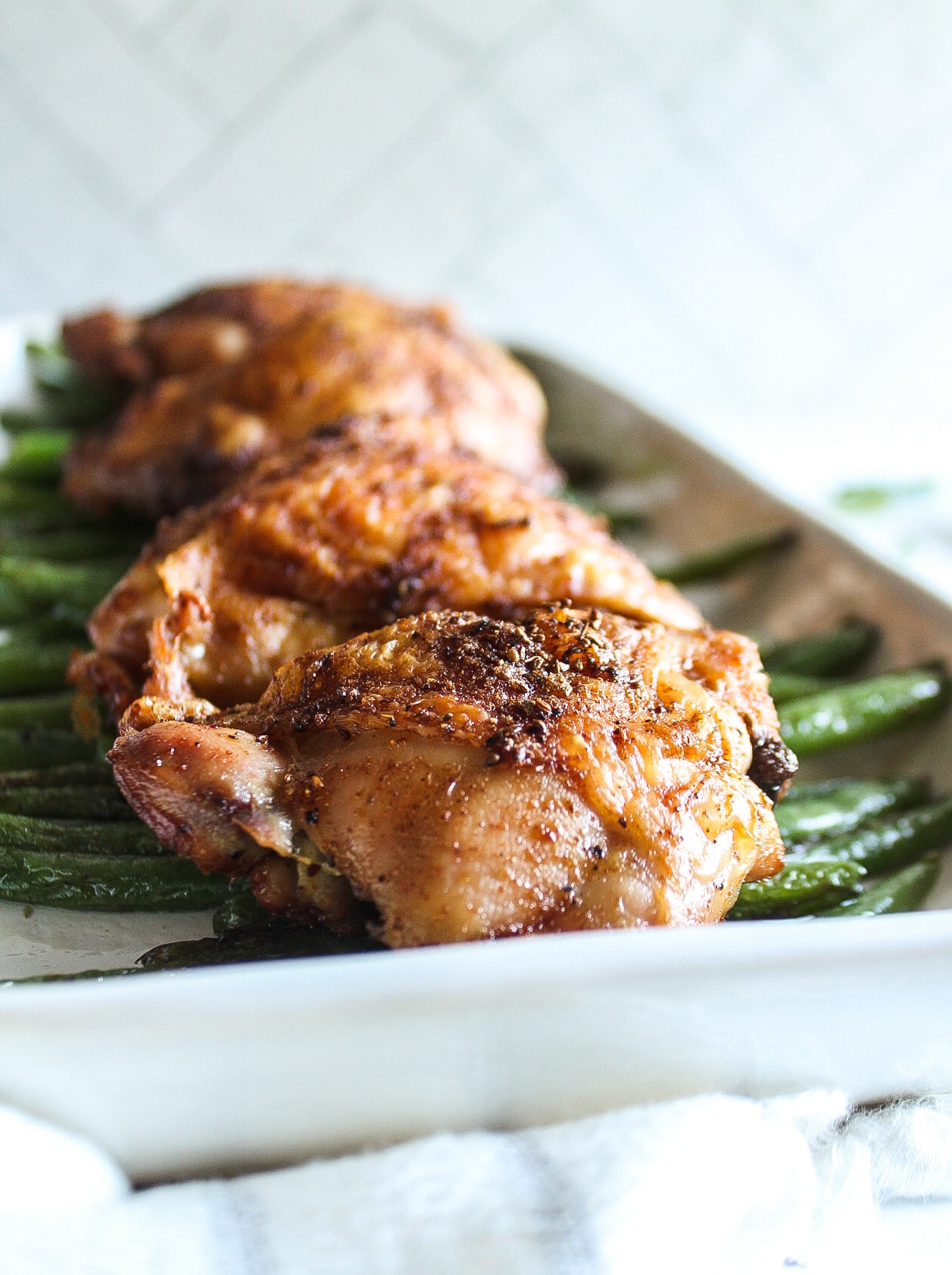 close up of a chicken thigh over string beans on a platter