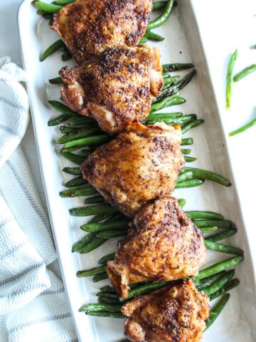 five roasted chicken thighs of a bed a sauteed string beans