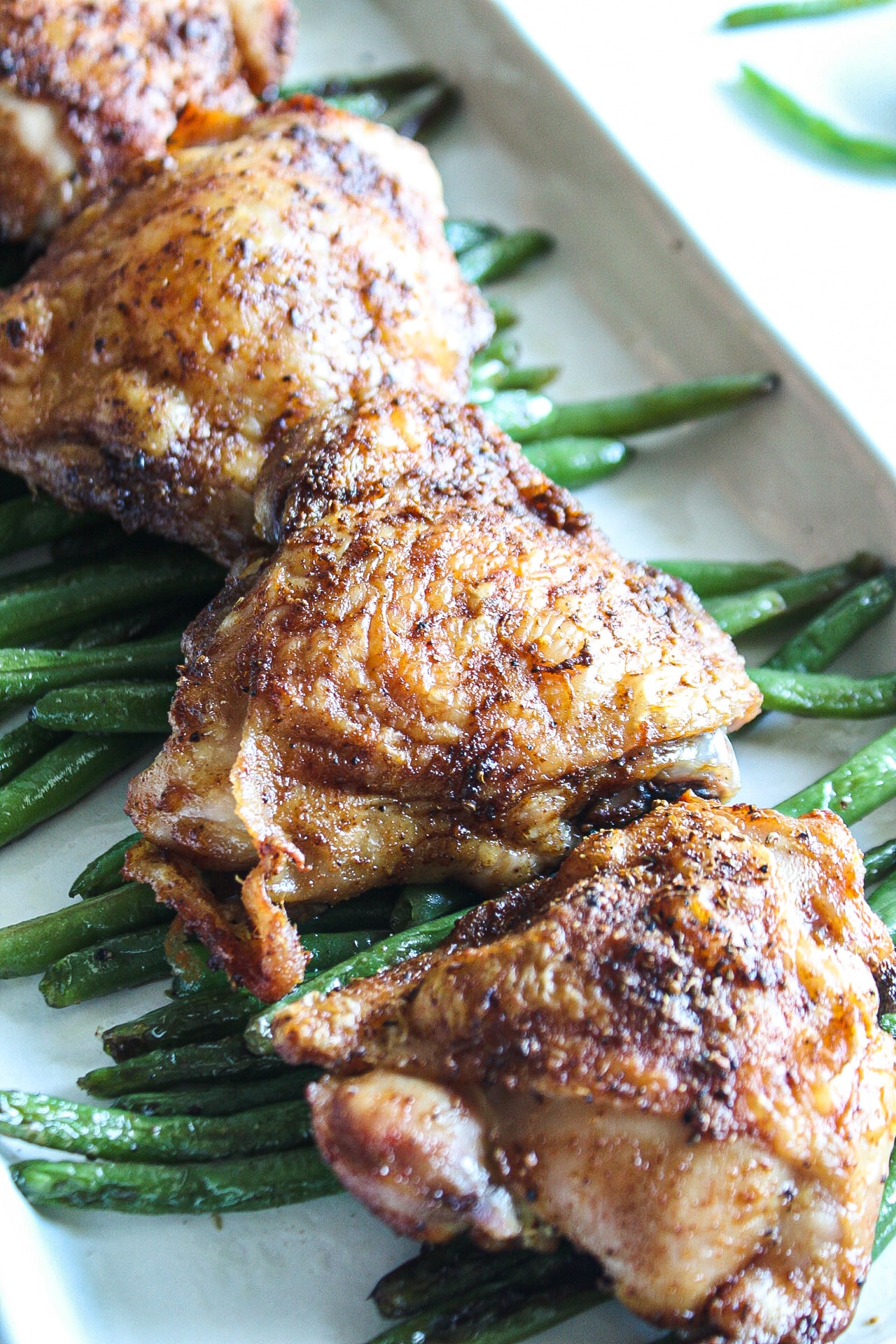 close up of a chicken thigh on a bed of string beans