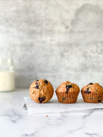 three blueberry muffins in a row with one of the tops the front