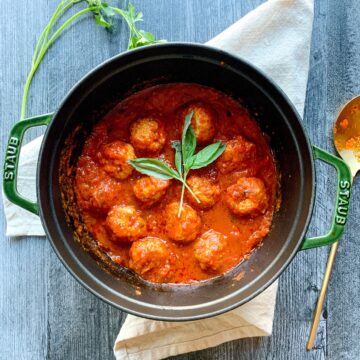 a pot of meatballs in tomato sauce with basil as garnish