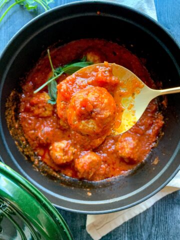 Italian chicken meatball on a gold spoon over a pot of meatballs in sauce