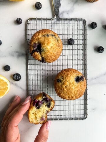 three lemon blueberry muffins with a hand holding a piece of the muffin