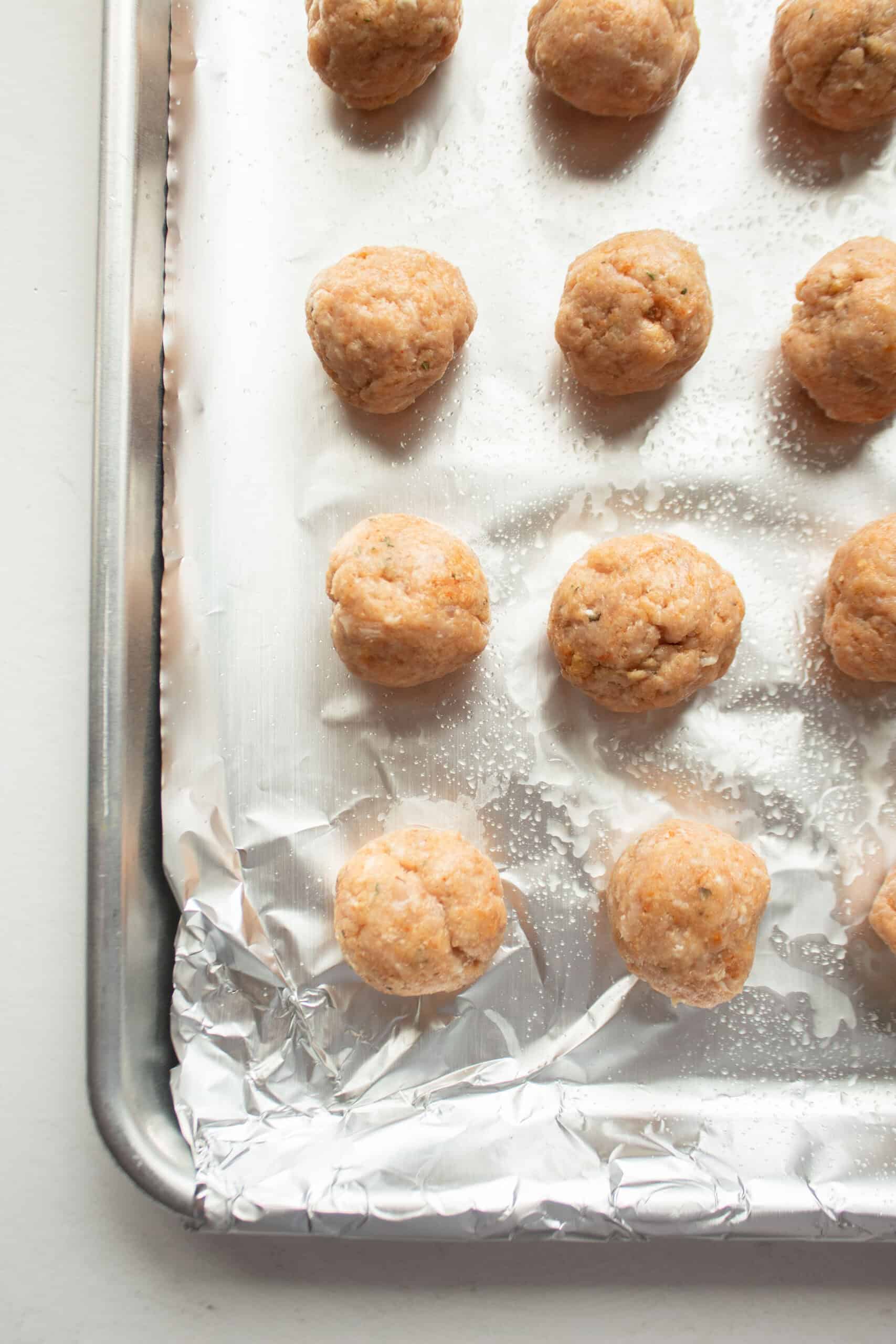 Mini chicken meatballs on a baking sheet.
