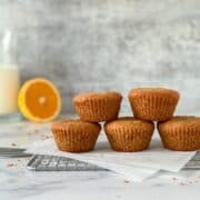 a stack of five orange chai muffins on a piece of parchment paper and a cooling rack with orange in the background