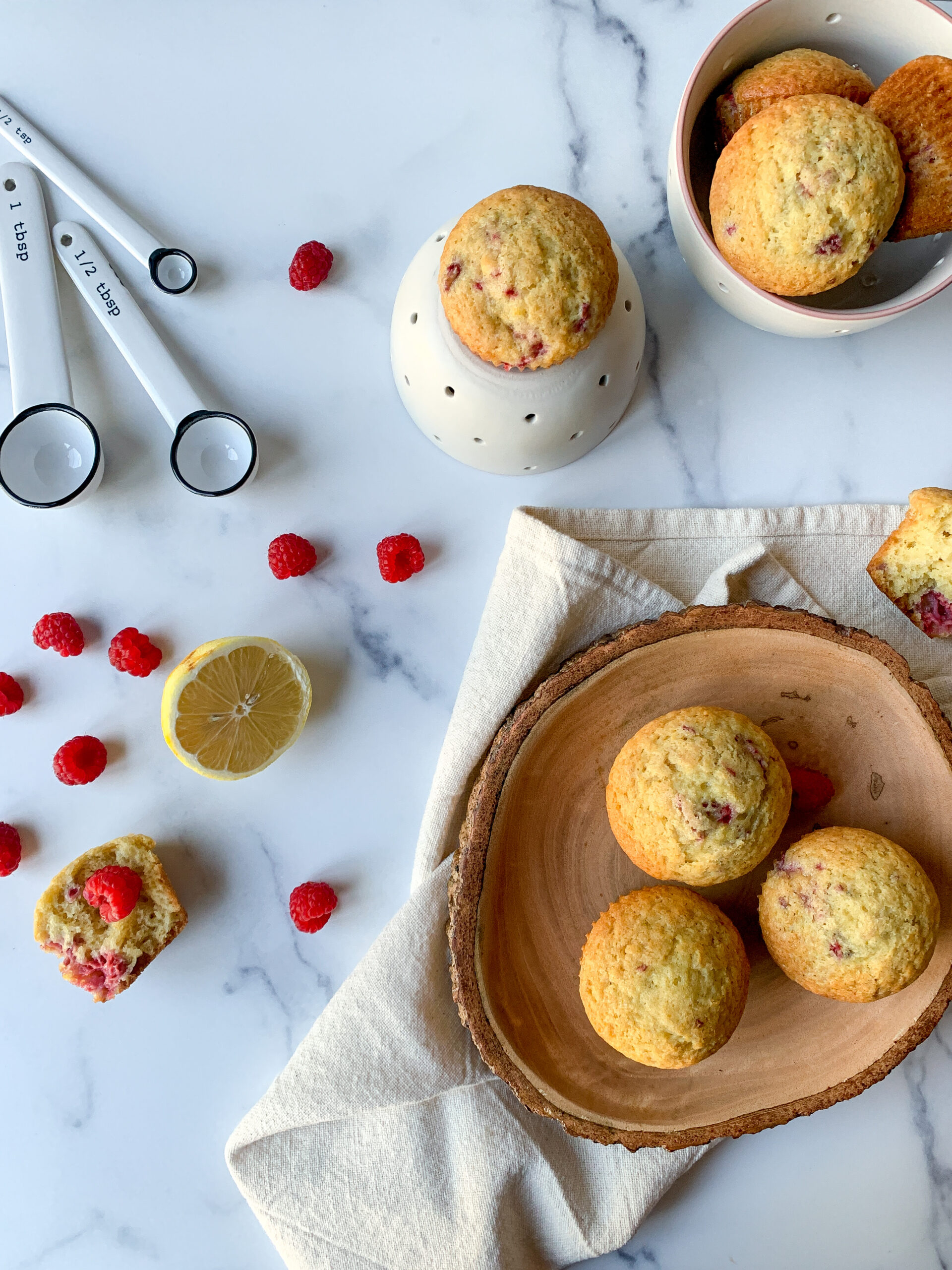an array of raspberry and lemon muffins with measuring spoons and raspberries and lemons surrounding them.
