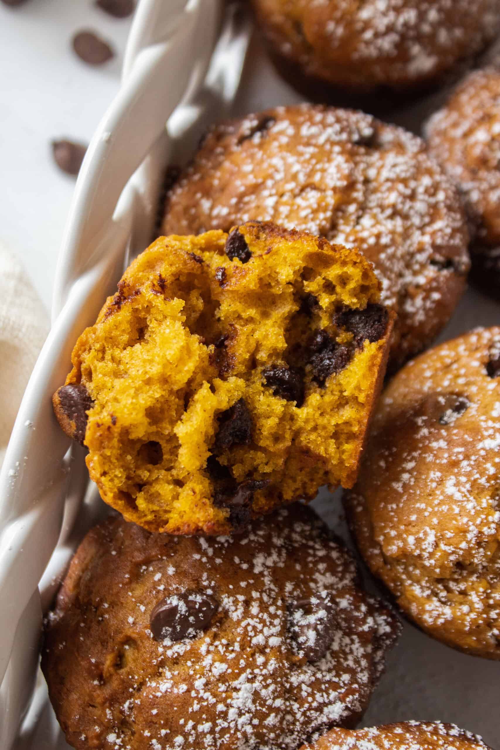 The inside of a pumpkin chocolate chip muffin laying on top of other muffins dusted with powdered sugar.