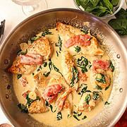 a large pan of tuscan chicken with basil and a glass of wine surrounding it