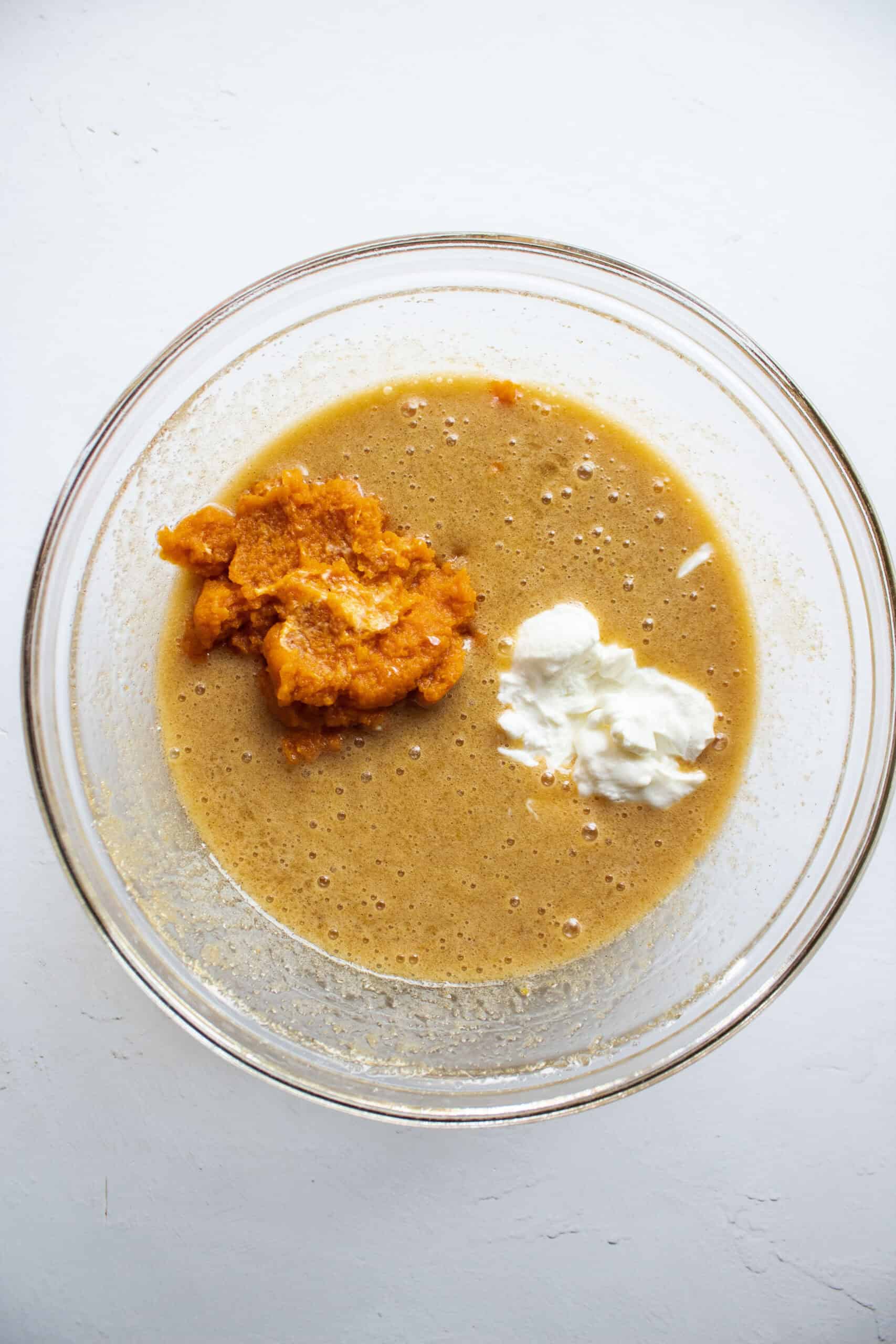 Wet ingredients in a medium mixing bowl with pumpkin puree and greek yogurt added to the batter.