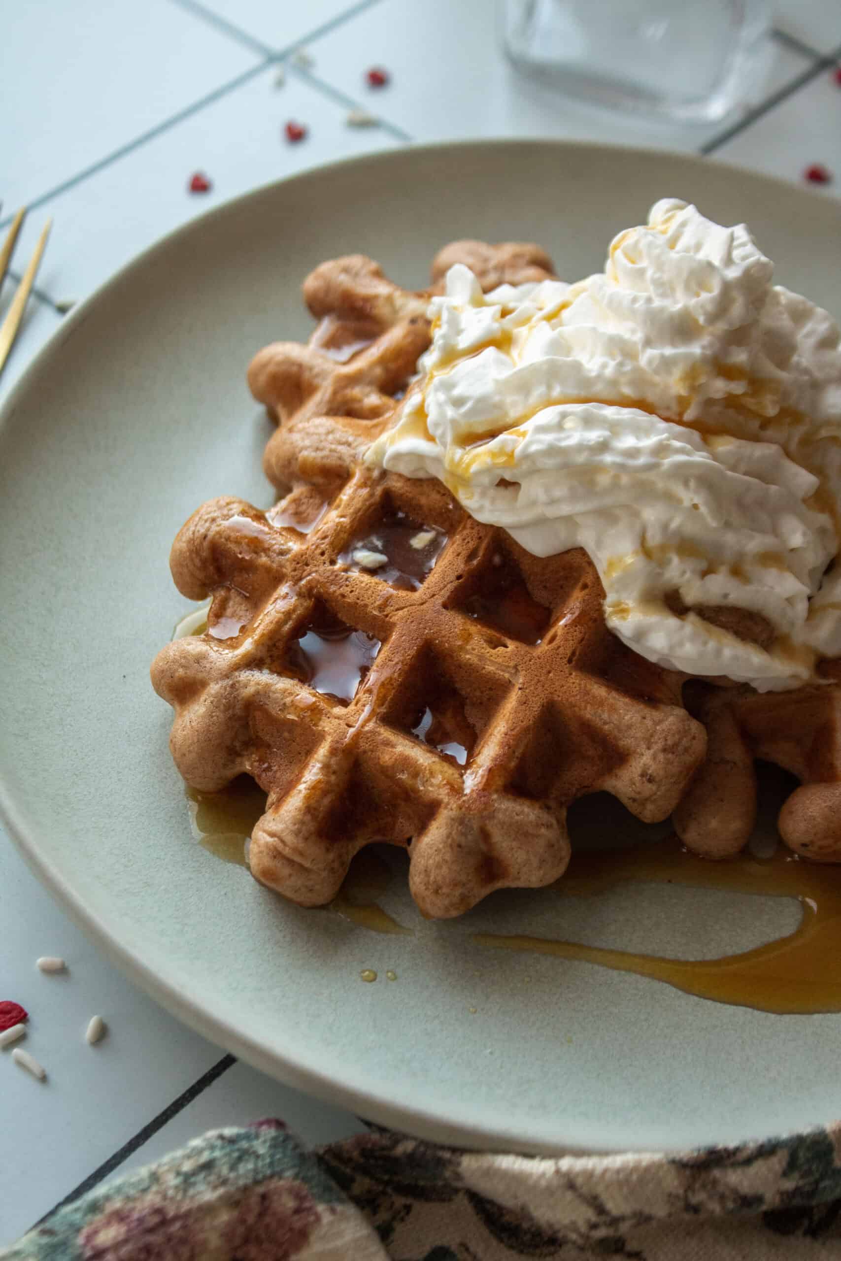 A closeup shot of a cocoa buttermilk waffle topped with whipped cream and syrup on a plate.