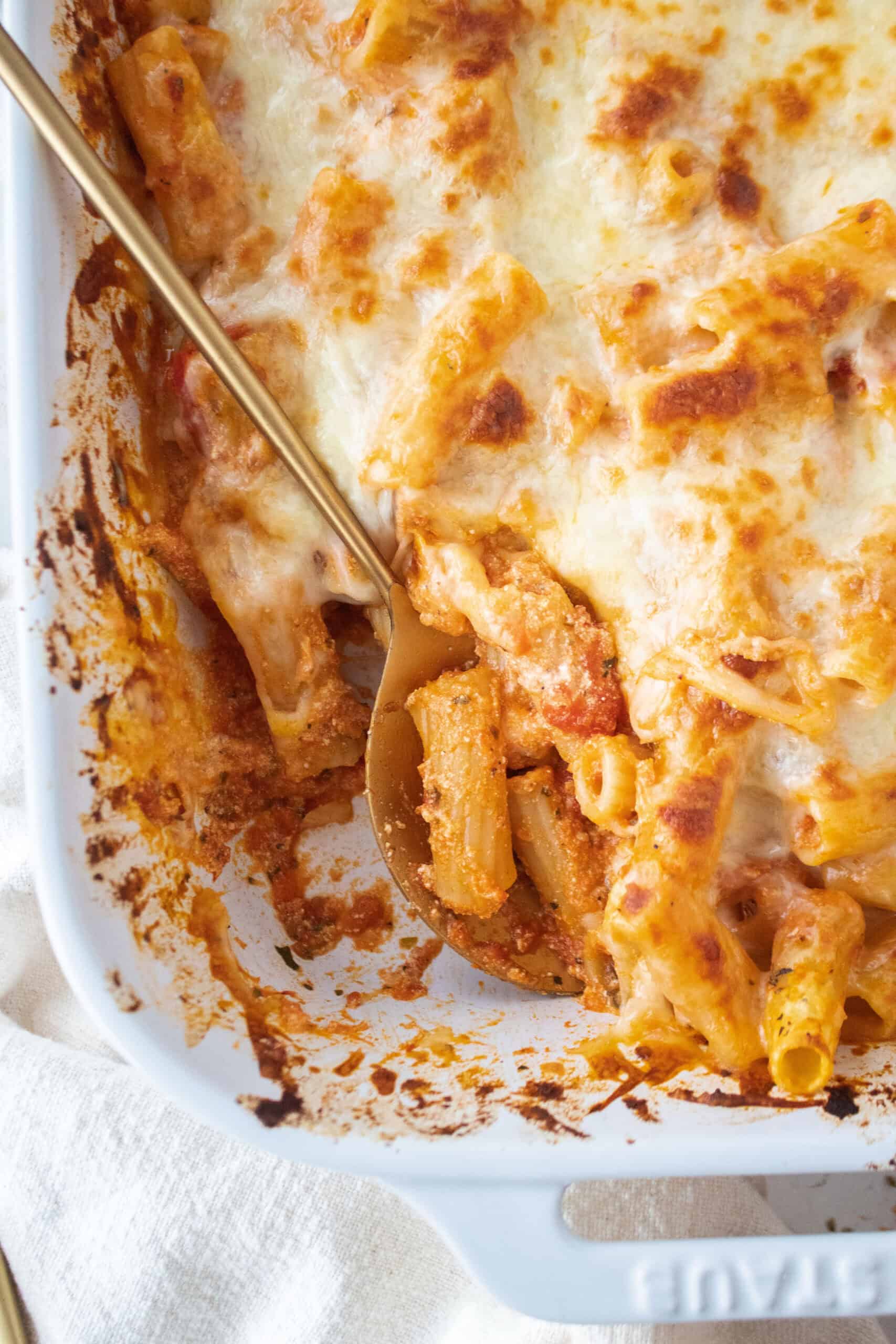 Close up of an easy baked ziti in a casserole dish with a gold spoon in the casserole.