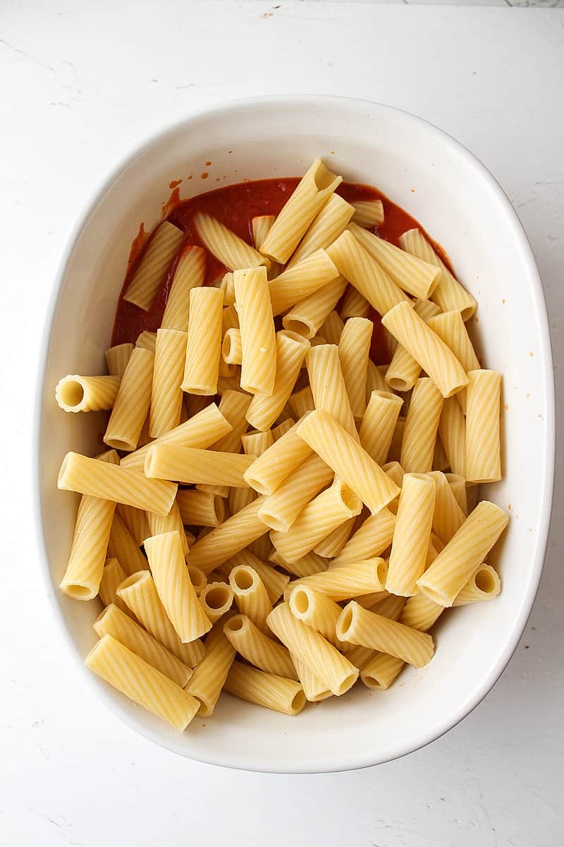 pasta in a casserole dish with marinara sauce underneath