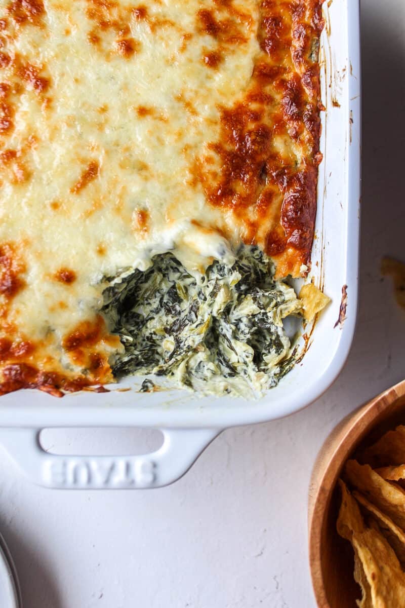a dish of spinach dip with some cheese missing