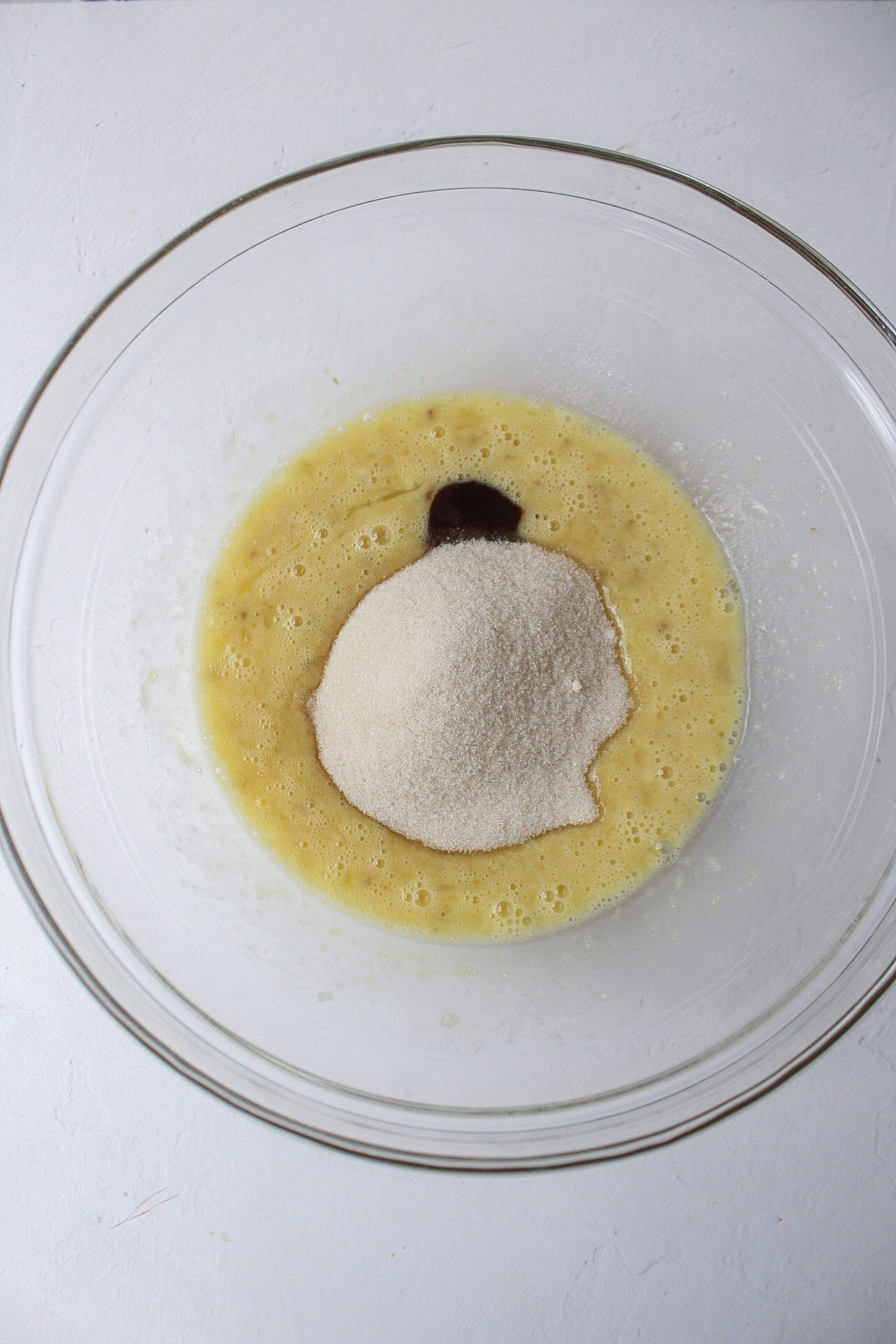 sugar and vanilla extract added to a bowl of whisked banana and egg.