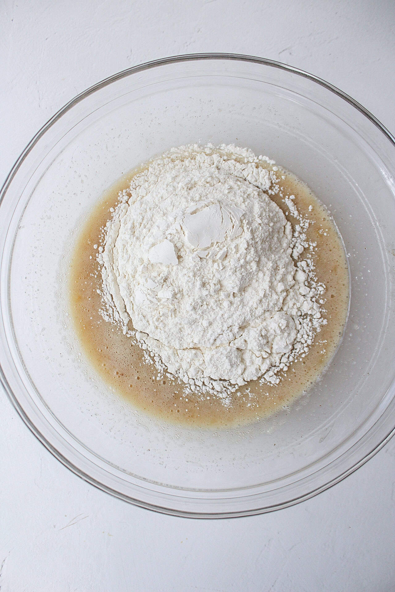 flour going into a bowl of whisked wet ingredients.