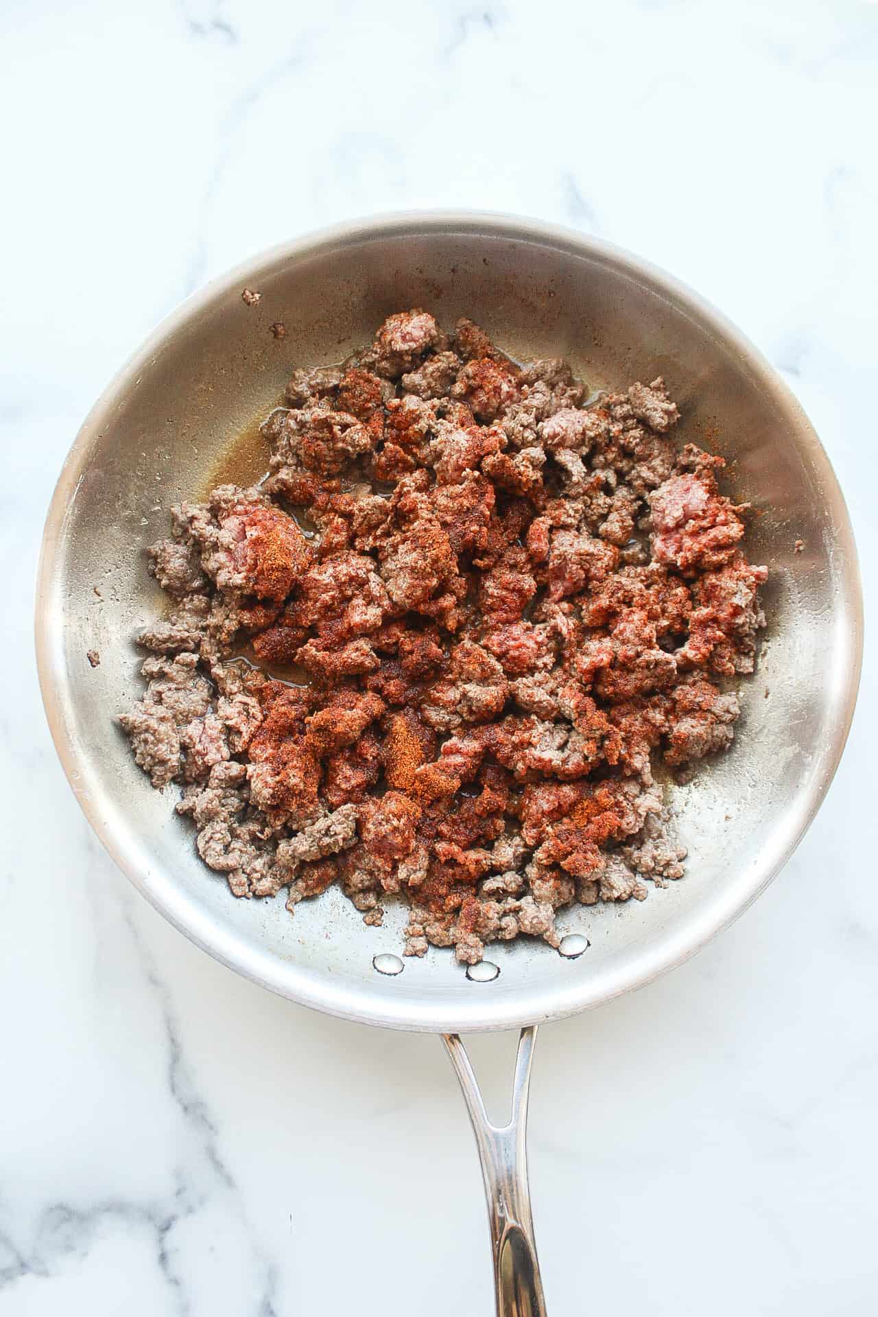 A frying pan of ground beef with seasoning on top.