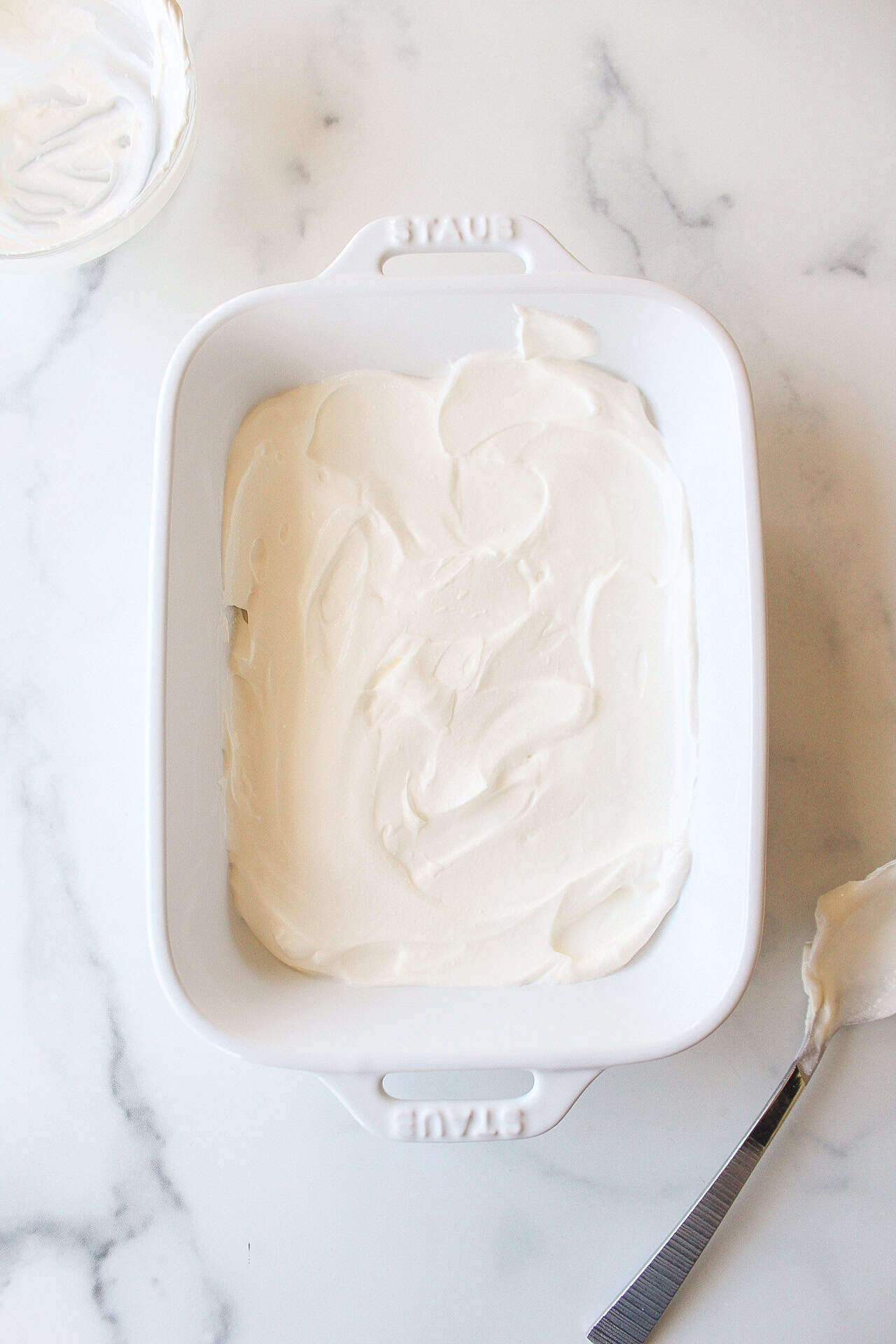 A small white baking dish with a layer of sour cream.