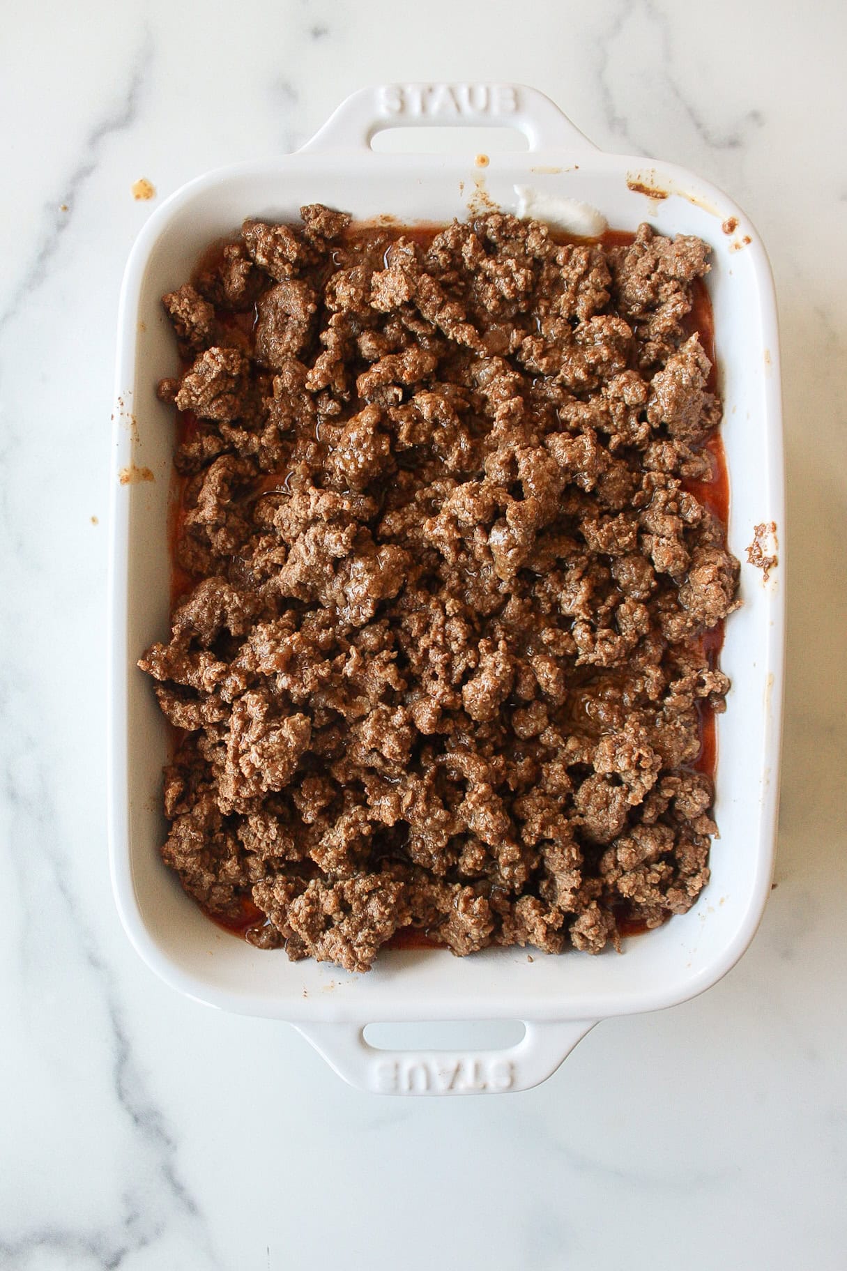 A baking dish with a layer of sour cream, salsa, and ground beef.