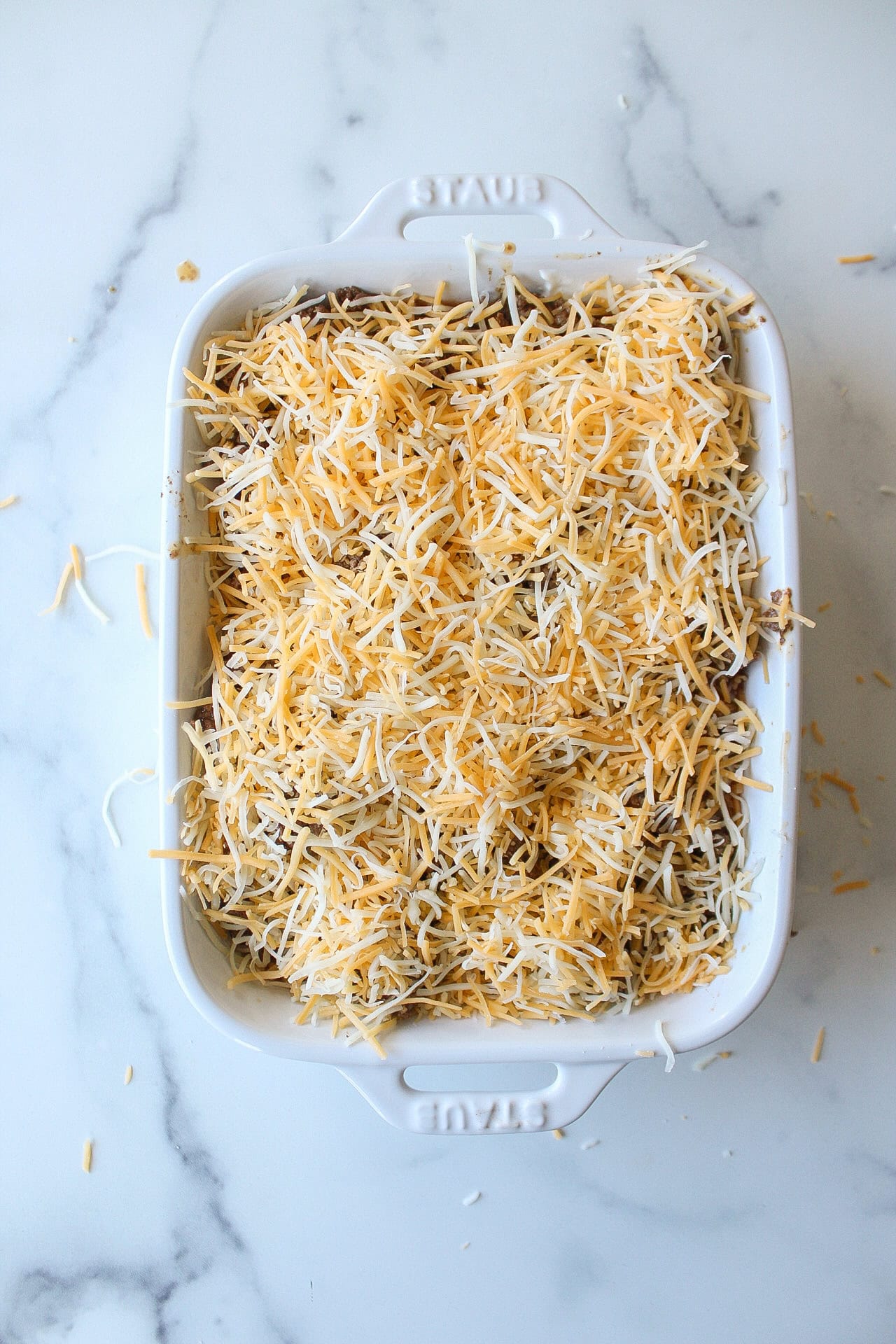 Shredded mexican cheese on top of a baking dish for a four layer taco dip.