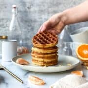 a hand holding a tilted syrup from the top of the waffle