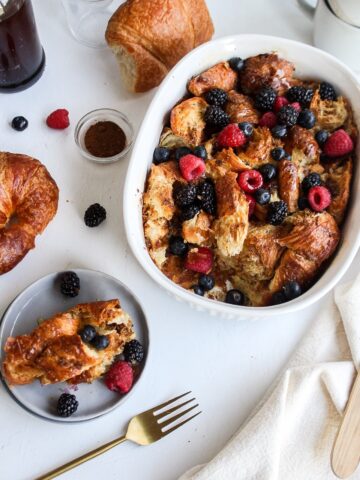 a croissant french toast bake with a few berries and croissants around the casserole dish