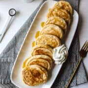 a platter with seven miniature pancakes with whipped cream on the side
