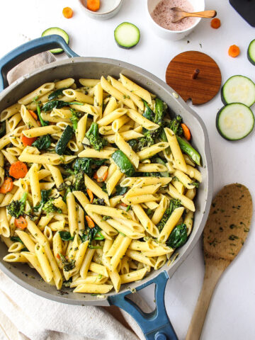 pasta and veggies in a pan with salt and a spoon around it