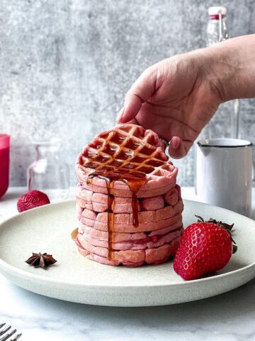 a hand tilting a pink waffle filled with syrup