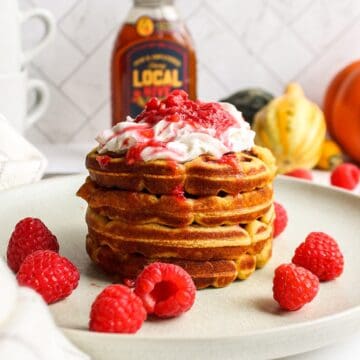 four pumpkin honey waffles stacked with whipped cream and honey