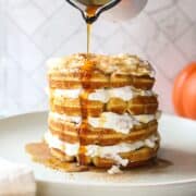 syrup being poured over a stack of waffles