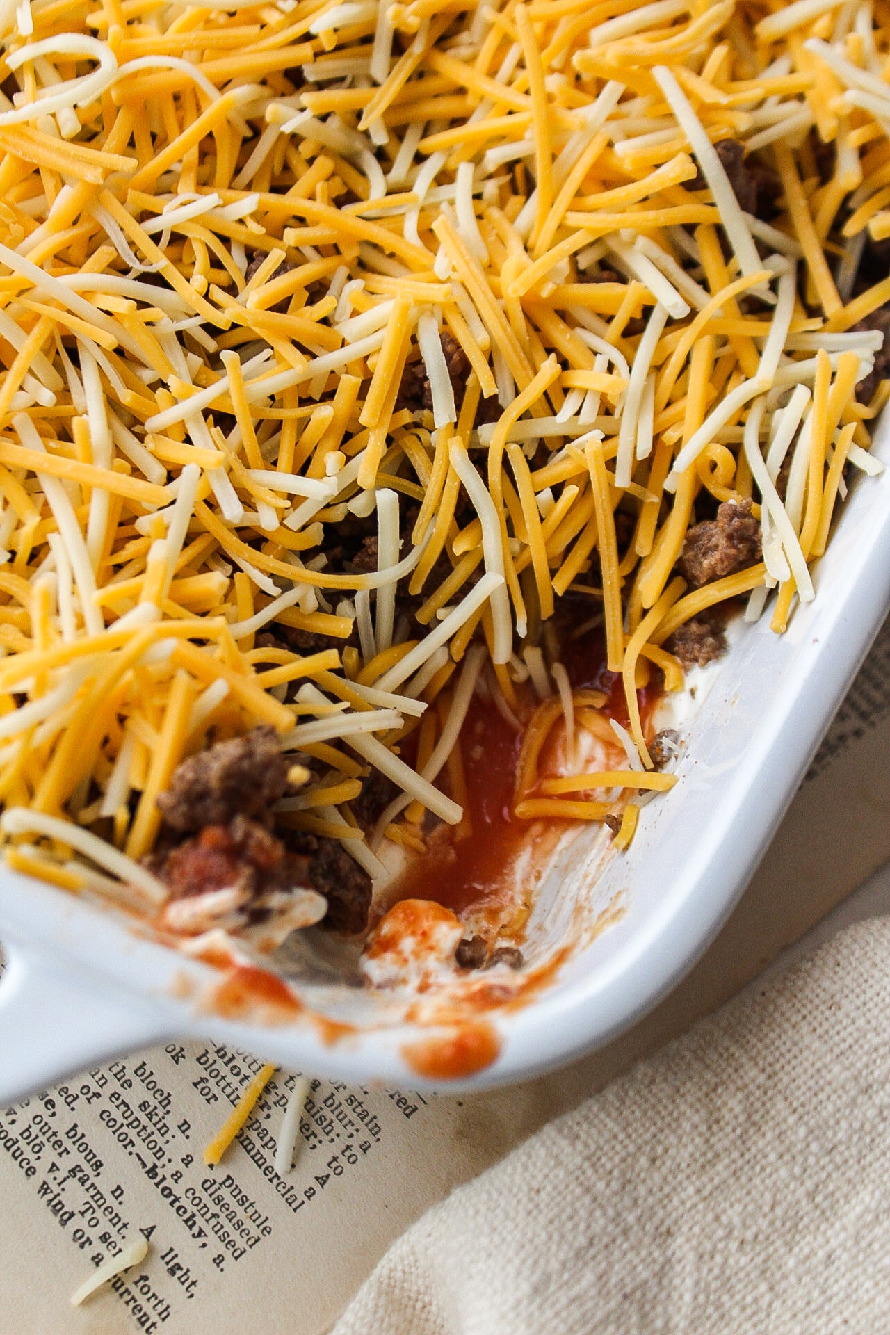 close up of a taco dip in a casserole dish with a portion of the dip scooped out