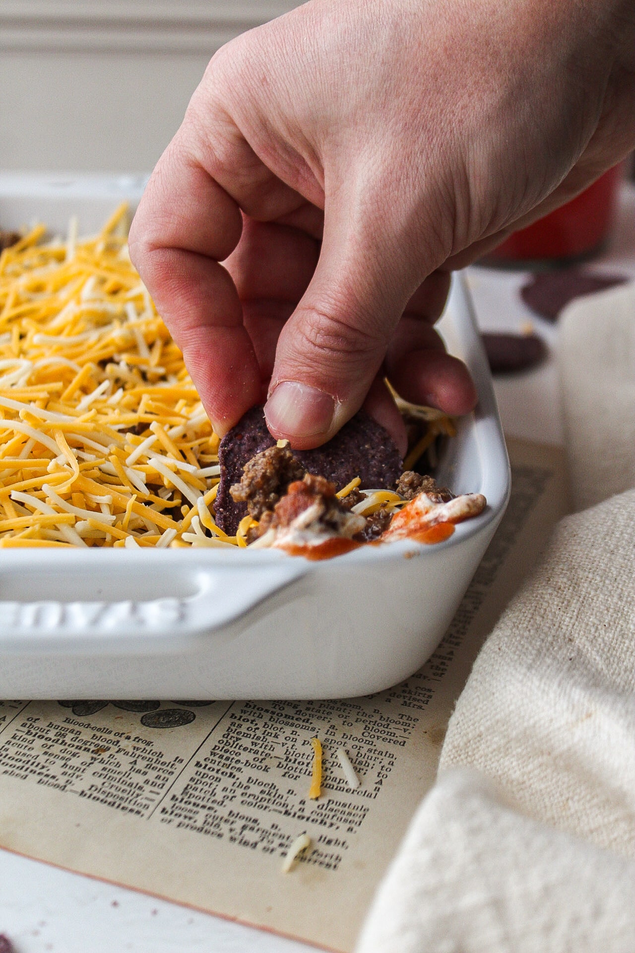 a hand reaching into the taco dip with a chip
