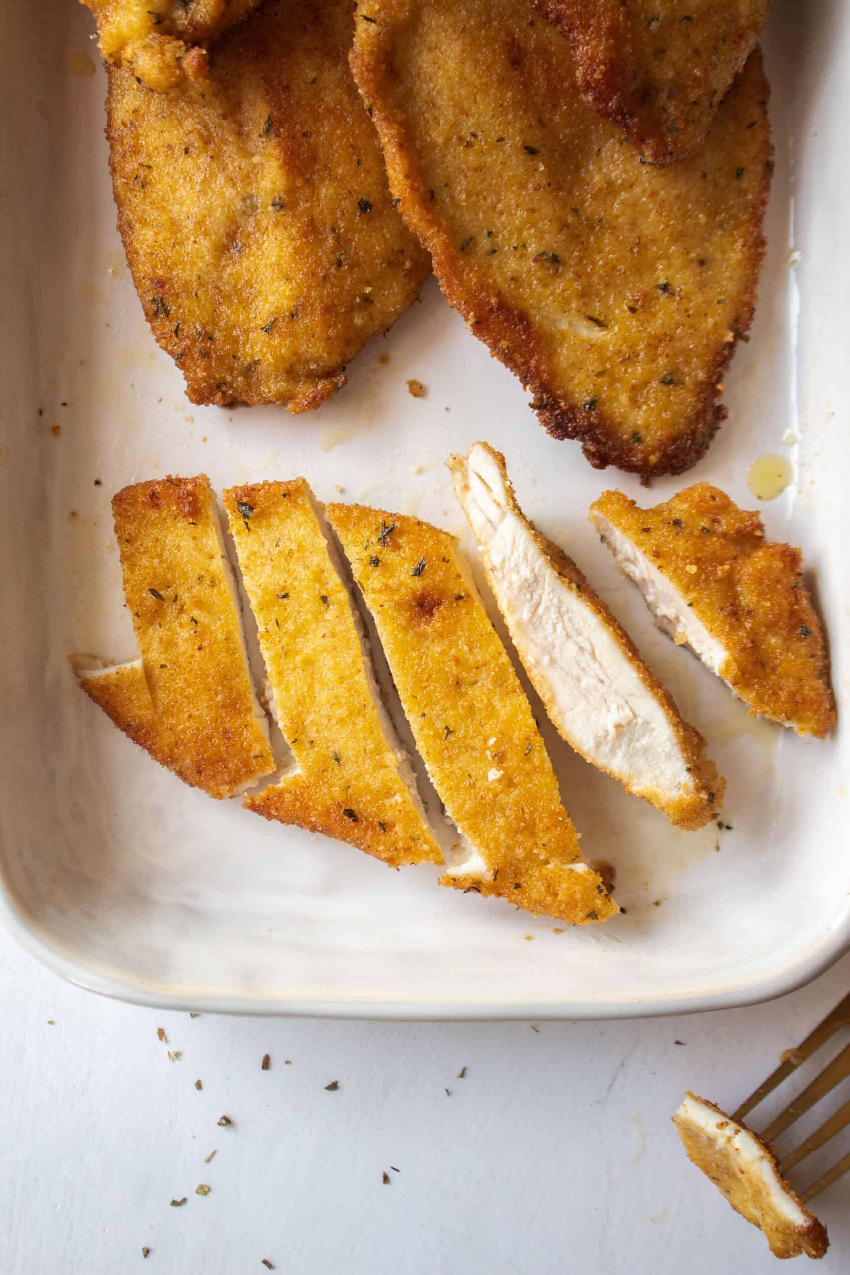 A cup up pan fried chicken cutlet on a platter surrounded by other chicken cutlets.