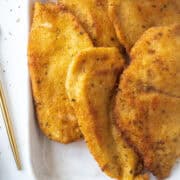Close up of a few pan fried chicken cutlets on a platter.