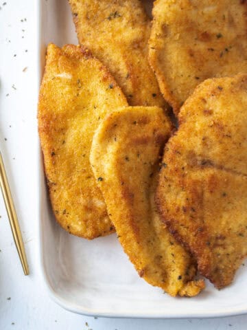 Close up of a few pan fried chicken cutlets on a platter.