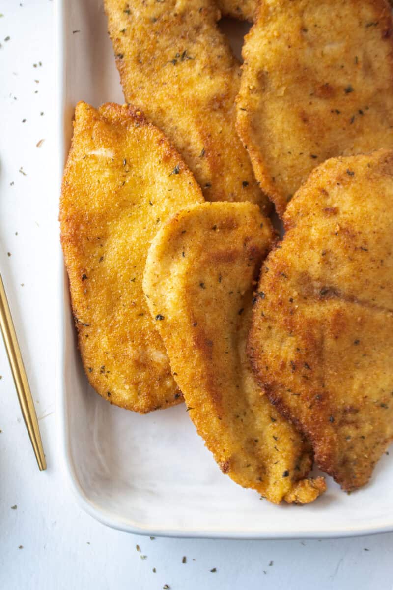 Close up of a few pan fried chicken cutlets on a platter.