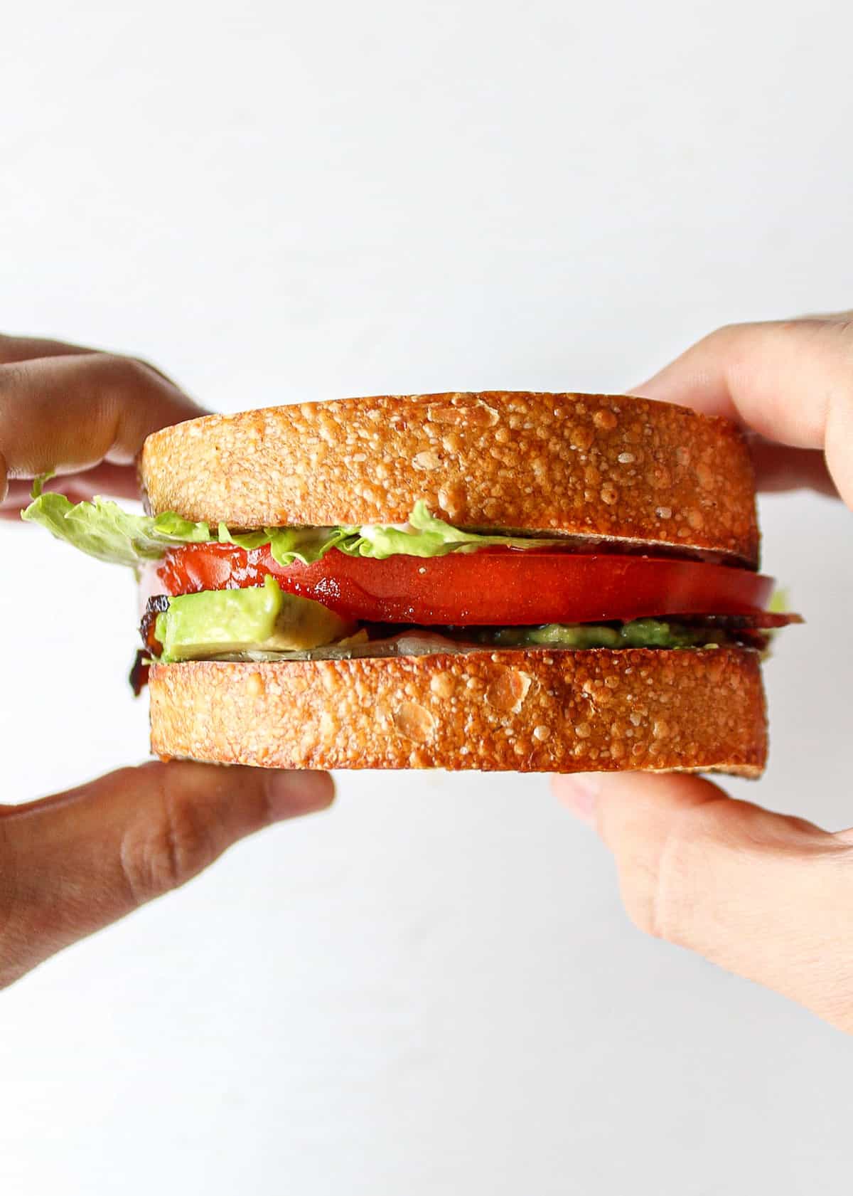 a BLT with avocado held between two hands