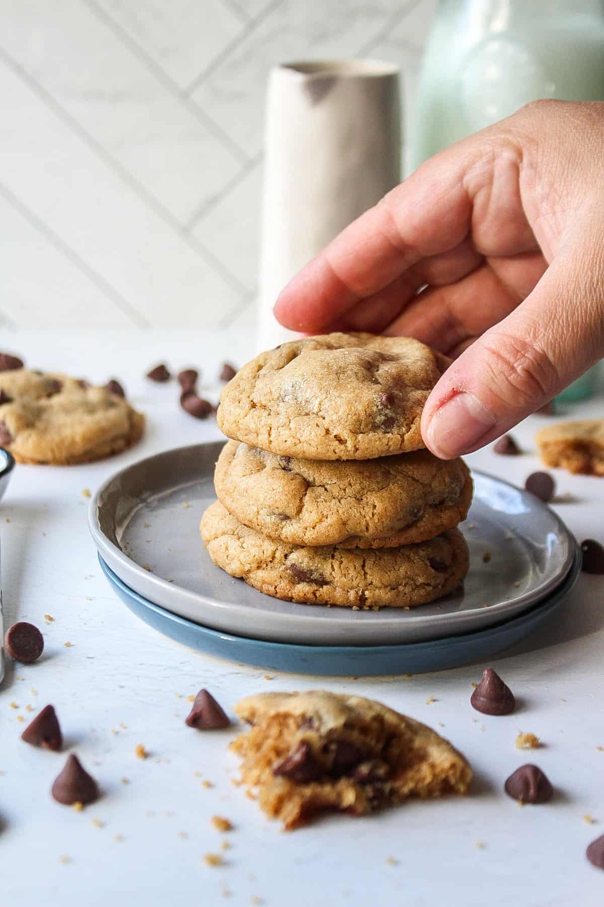 brown butter chocolate chip cookies stacked on a small plate with a hand reaching in to grab a cookie