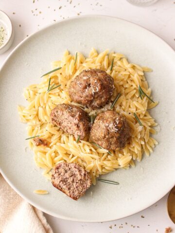 four meatballs on a bed a orzo with one of the meatballs cut open