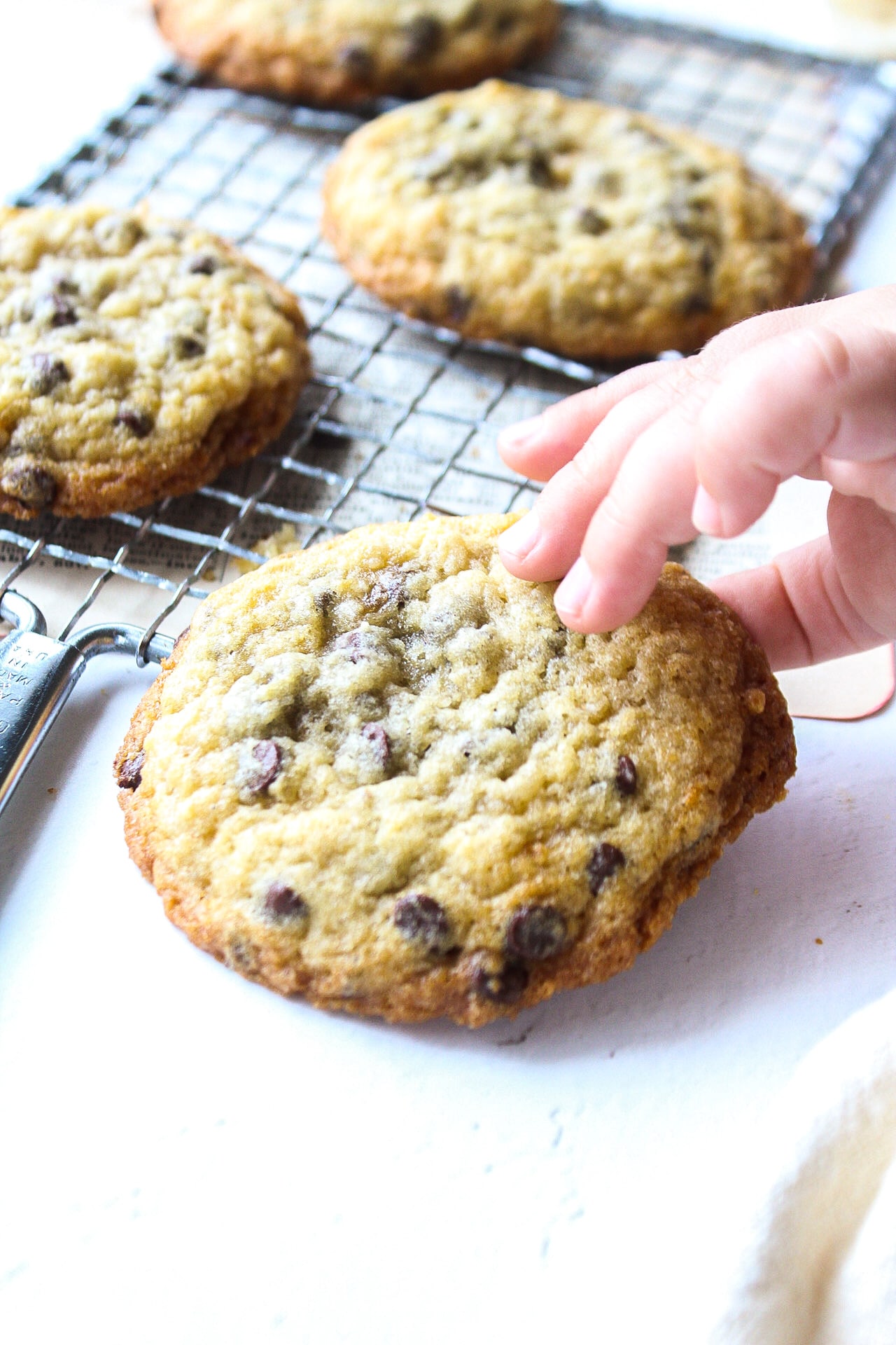 a banana bread cookie on a cooling rack with a tiny hand grabbing the cookie