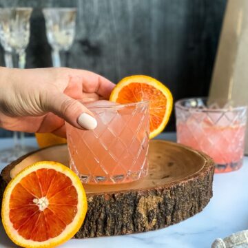 a hand grabbing a glass of a blood orange margarita