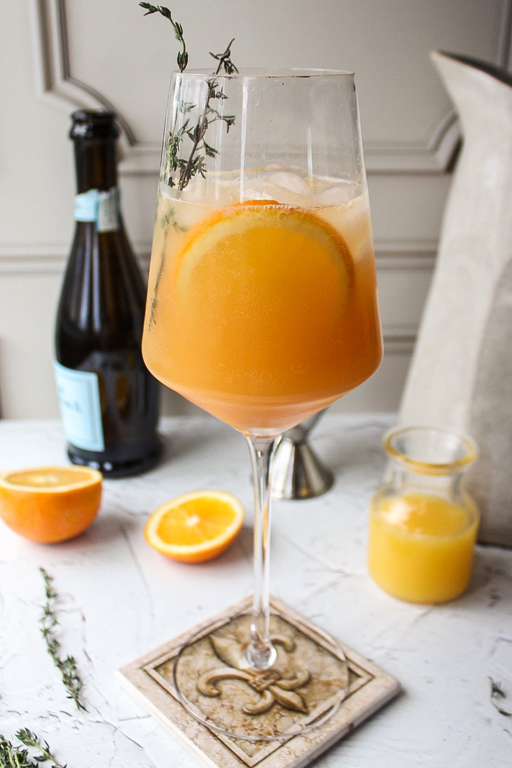 a glass of an orange cocktail with orange slices and a bottle of champagne in the background