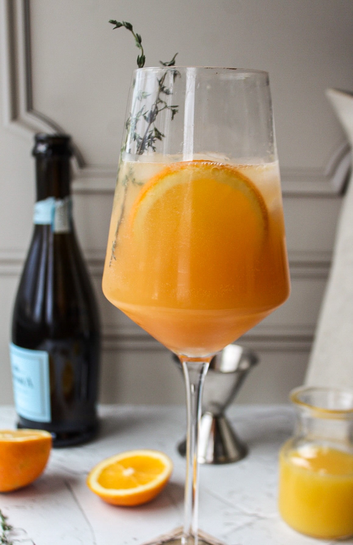 a glass of an orange cocktail with orange slices and a bottle of champagne in the background